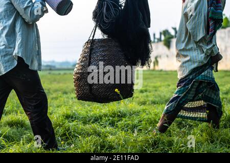 Two people carrying a bamboo fish basket with a fishing net before the evening Stock Photo