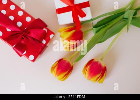 Bouquet of beautiful spring tulips in vase and gift box on table against light background. International Women's Day and Valentine Day Stock Photo