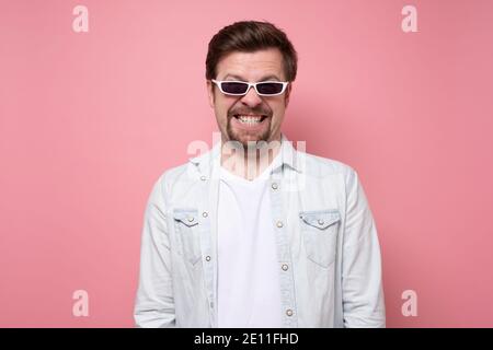 Studio shot of young handsome man in sunglasses smiling on pink wall. Stock Photo