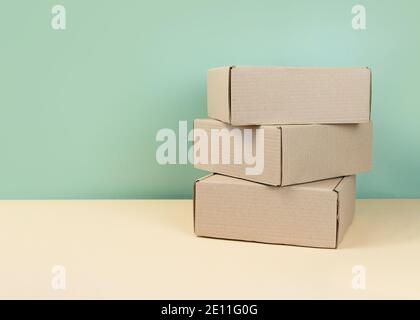 Stack of Brown cardboard boxes on mint background. Blank carton box. Gifts packaging concept. Craft box for gift or present on neutral backdrop Stock Photo