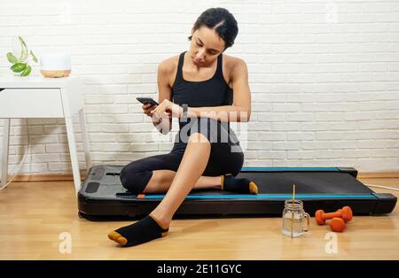 Young mixed-raced woman measures activity control with smartphone after workout at home Stock Photo