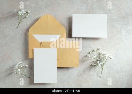 Blank paper cards, envelopes, flowers on concrete table. Wedding invitations mockups. Flat lay, top view. Stock Photo