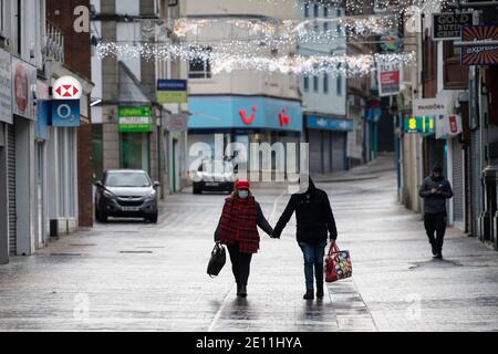 MERTHYR TYDFIL, WALES - JANUARY 03: A man and woman walk down Merthyr high street holding hands and wearing face masks on January 03, 2021 in Merthyr Stock Photo