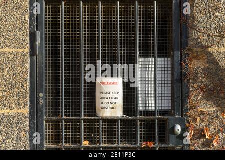 Fire exit please keep clear sign on a black metal door and stone wall frame Stock Photo