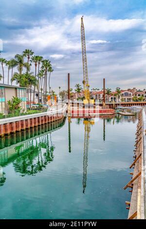 Yellow crane and docks on canal in Long Beach California against cloudy blue sky Stock Photo