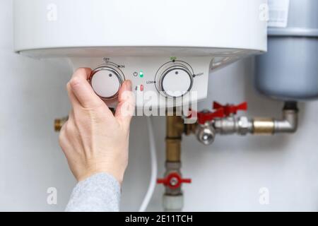 Female hand turning on electric water heater (boiler). Household enegry saving equipment Stock Photo