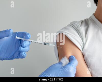 Close-up on hands in gloves with syringe and shoulder of the patient, teen kid. Covid 19, flu or measles vaccine concept. Medic, doctor or nurse Stock Photo