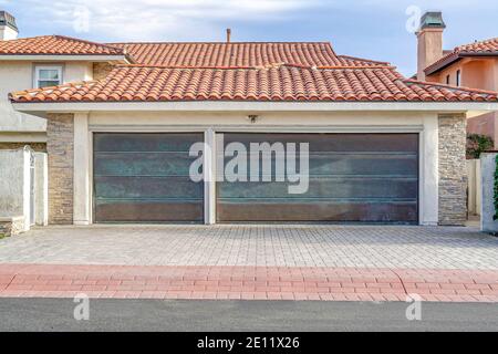 House with metal doors on garage with red tile roof and brick paved driveway Stock Photo