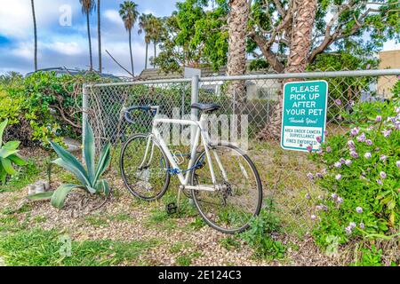 Bicycle against fence with Pick Up After Your Pet sign in San Diego, California Stock Photo