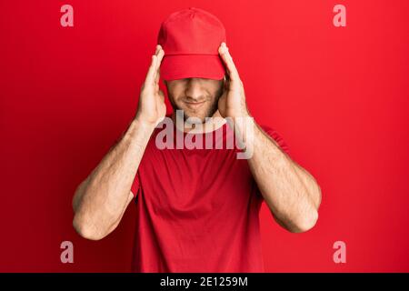 Young caucasian man wearing delivery uniform and cap suffering from headache desperate and stressed because pain and migraine. hands on head. Stock Photo