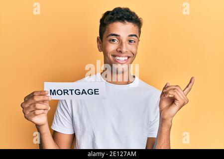 Young handsome african american man holding mortgage word smiling happy pointing with hand and finger to the side Stock Photo