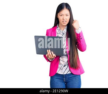 Young beautiful chinese woman using laptop annoyed and frustrated shouting with anger, yelling crazy with anger and hand raised Stock Photo
