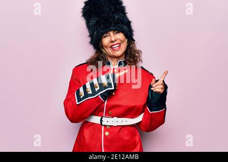 Middle age beautiful wales guard woman wearing traditional uniform over pink background smiling and looking at the camera pointing with two hands and Stock Photo