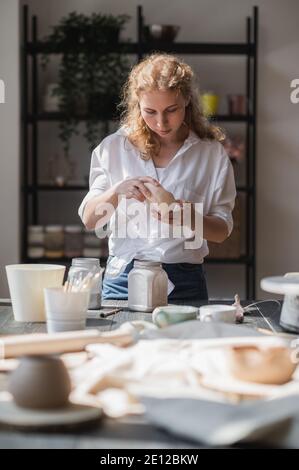 Girl draws on a clay bowl. Female potter works in her studio glazing ceramic pot. Stock Photo