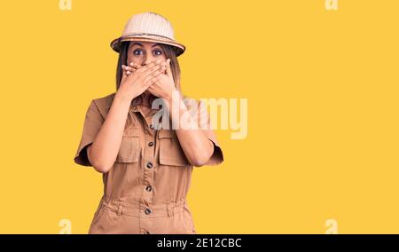 Young beautiful woman wearing explorer hat shocked covering mouth with hands for mistake. secret concept. Stock Photo