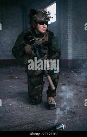 Military man armed with assault rifle running through smoke in abandoned building area Stock Photo