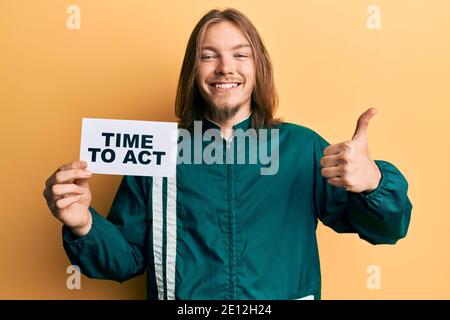 Handsome caucasian man with long hair holding time to act banner smiling happy and positive, thumb up doing excellent and approval sign Stock Photo