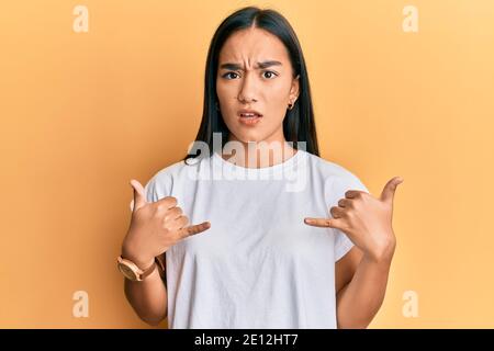 Young asian woman doing shaka sign with hands clueless and confused expression. doubt concept. Stock Photo