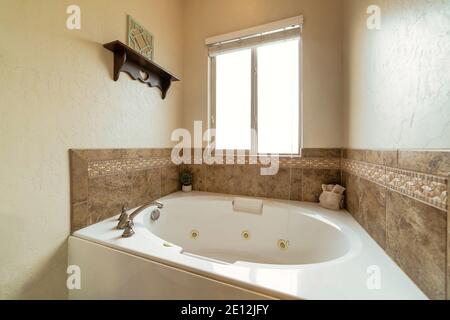 Round white built in bathtub against warm toned tiles and plain beige wall Stock Photo