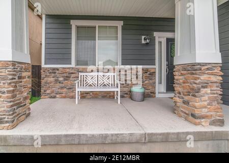 Home facade with white bench on porch against gray siding and stone brick wall Stock Photo