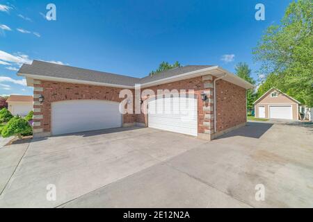 Building with red brick wall gray roof and two white arched wooden garage doors Stock Photo