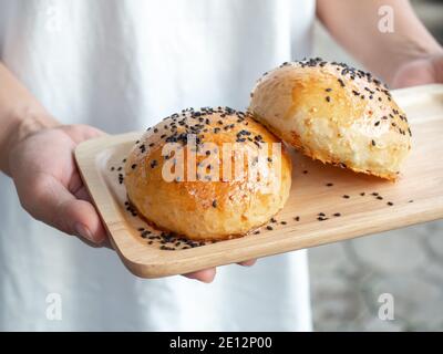Two fresh homemade burger buns topped with black sesame seed on small wooden tray serving hands for breakfast. Two tasty sweet sandwich round buns jus Stock Photo