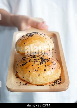 Two fresh homemade burger buns topped with black sesame seed on small wooden tray serving hands for breakfast, vertical style. Two tasty sweet sandwic Stock Photo