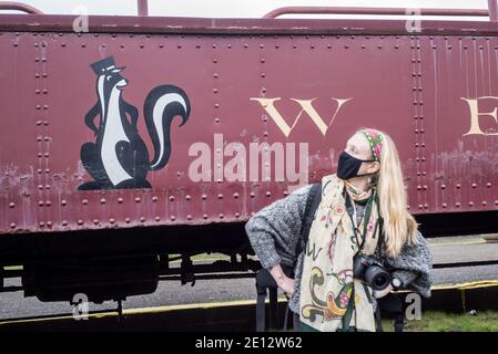 A woman in a facemask faces off with the skunk train mascot, a skunk conductor, in fort bragg, California. Stock Photo