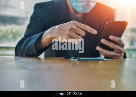 Businessman in face mask using mobile smartphone to working online focus on hand Stock Photo