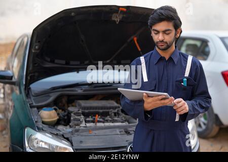 A MECHANIC USING A DIGITAL TABLET TO CHECK THE WORKING OF A CAR Stock Photo