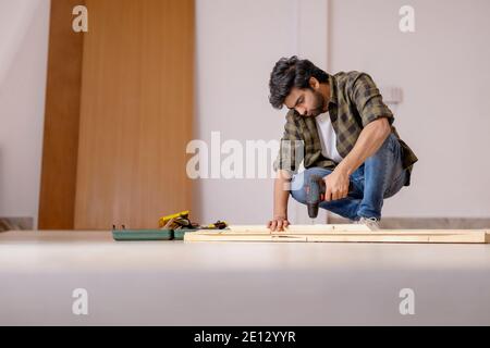 A CARPENTER SITTING ON FLOOR AND DRILLING WOOD Stock Photo