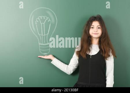 Pre-adolescent girl holding painted electric bulb. On school board background. High resolution photo. Full depth of field. Stock Photo