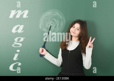 Pre-adolescent wizard girl holding painted magic stick. On school board background. High resolution photo. Full depth of field. Stock Photo