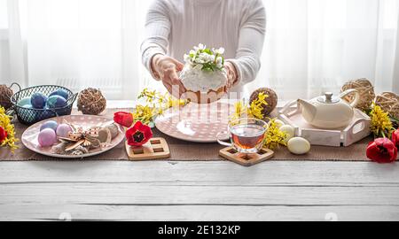 Easter composition with cake in female hands, tea, flowers, eggs and decor details. Easter family holiday concept. Stock Photo