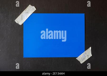 Rectangular sheet of blue paper glued with adhesive tape to a black background. Minimalistic multitask background. Stock Photo