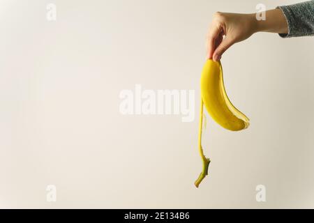 Hand of unknown caucasian woman holding banana peel in front of white wall - copy space concept of ending and finish trash ready to be thrown away old Stock Photo