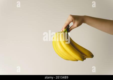 Close up on hand of unknown caucasian woman holding bananas in front of white wall - healthy organic food fresh fruit concept copy space Stock Photo