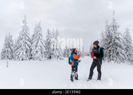 Mother and son drinking hot tea in winter conditions in snow covered landscape Stock Photo