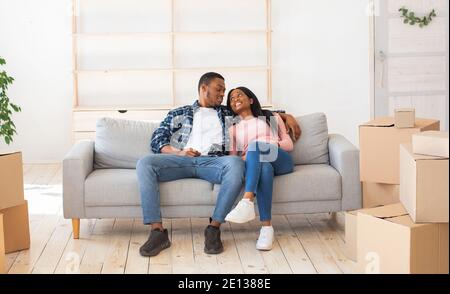 Cheerful millennial family moving to new property, taking break from unpacking, resting on sofa among carton boxes Stock Photo