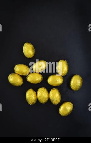 Small group of gold yellow easter mini eggs which are foil wrapped. The are on a black and grey background, with copy space around. Stock Photo