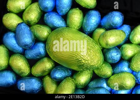 Pile group of multi coloured and different sizes of colourful foil wrapped chocolate easter eggs in blue, yellow and lime green with a large green egg. Stock Photo