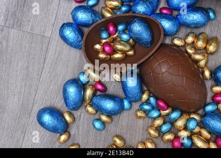 Pile or group of multi colored and different sizes of colourful foil wrapped chocolate easter eggs in pink, blue, gold and green. Large egg halves. Stock Photo