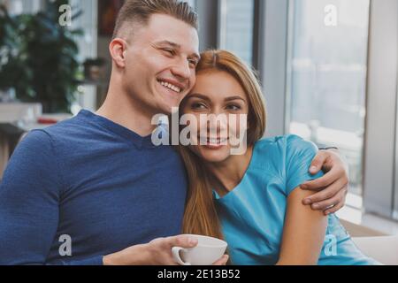 Handsome man smiling, cuddling with his beautiful girlfriend at the restaurant. COuple hugging, while drinking morning coffee at the cafe. Beautiful w Stock Photo