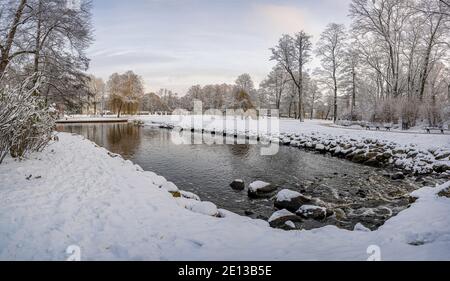 Panoramic winter landscape in snowy park with beautiful small pond and covered in snow trees. Stock Photo