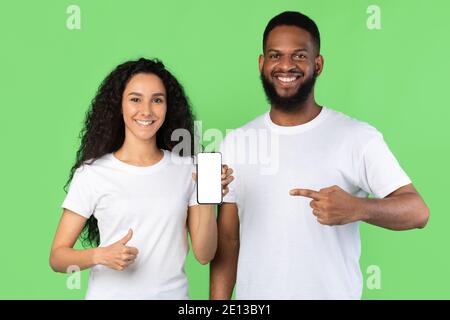 Couple Showing Phone Empty Screen Gesturing Thumbs-Up Over Green Background Stock Photo
