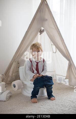 Cute toddler child, boy, sitting on a baby toilet potty, playing with toys Stock Photo