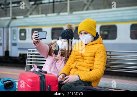 Two children are sitting on the platform waiting for the train. The girl takes a selfie. Stock Photo