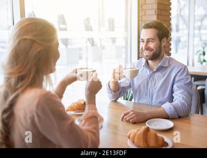 Cheerful young guy having coffee together with his girlfriend at cafe, chatting and smiling during breakfast Stock Photo