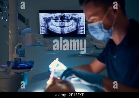 Dentist examining patient with dental equipments against modern dental surgery with x-ray. Stock Photo