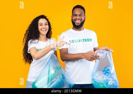 Multicultural Volunteers Picking Plastic In Garbage Bags Over Yellow Background Stock Photo